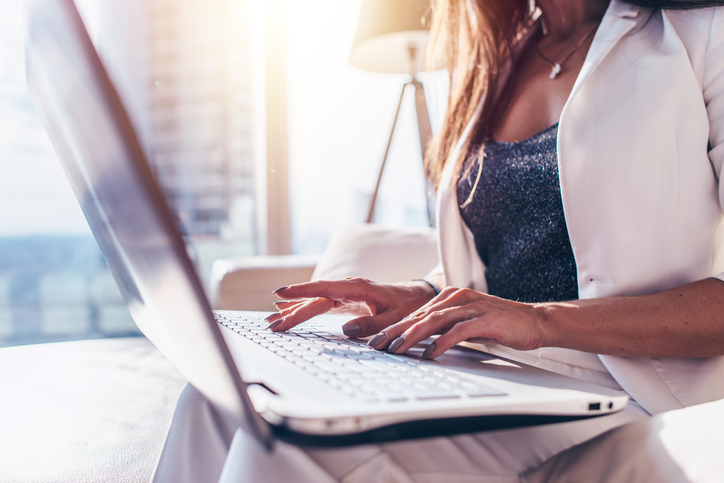 Close-up image of female hands typing on laptop keyboard in modern office